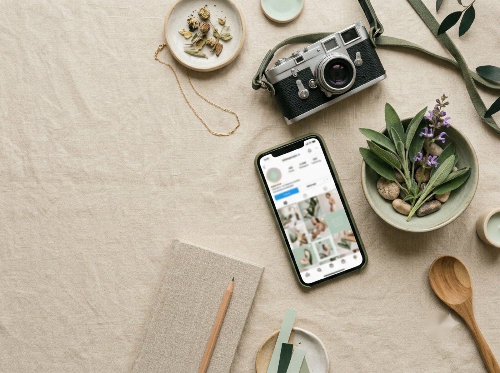Flat lay con un teléfono mostrando un feed de Instagram de clínica, una cámara y flores de salvia.